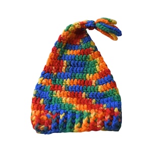 May include: A colorful, handmade crochet hat in a pointed shape. The hat features a vibrant mix of red, orange, yellow, green, and blue yarn. The top of the hat has a small, knotted tassel. The hat is likely for a child.