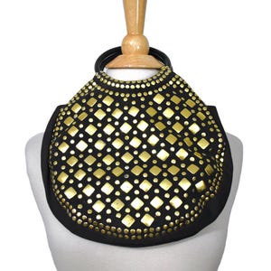 May include: A black handbag featuring a circular silhouette and two black rounded handles. The front surface is densely decorated with a repeating pattern of gold-toned metal studs, including both square-shaped and small circular accents.