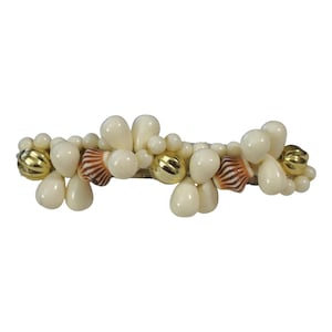 May include: A decorative hair accessory featuring a cluster of off-white, teardrop-shaped beads, interspersed with small, round beads, gold-colored orbs, and small seashells. The accessory is designed to be worn in the hair.