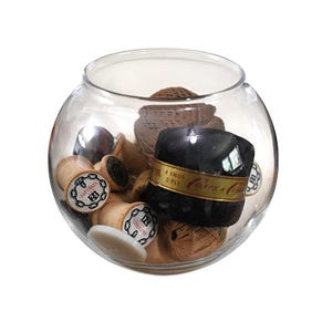 May include: A clear glass bowl filled with various sewing supplies, including wooden spools labeled J&P Coats 24, a black spool with gold text reading 4 ENDS 2 PLY Coats & Clark, brown thread balls, and a white button, all contained within the rounded vessel.