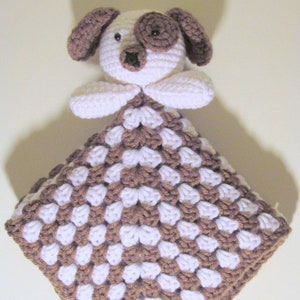 May include: A crocheted brown and white puppy security blanket with a brown nose and black eyes.