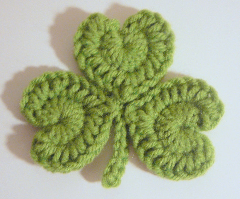 May include: A green crocheted shamrock with three leaves and a stem.