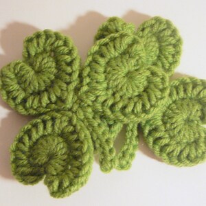 May include: A green crocheted four-leaf clover with a textured design.