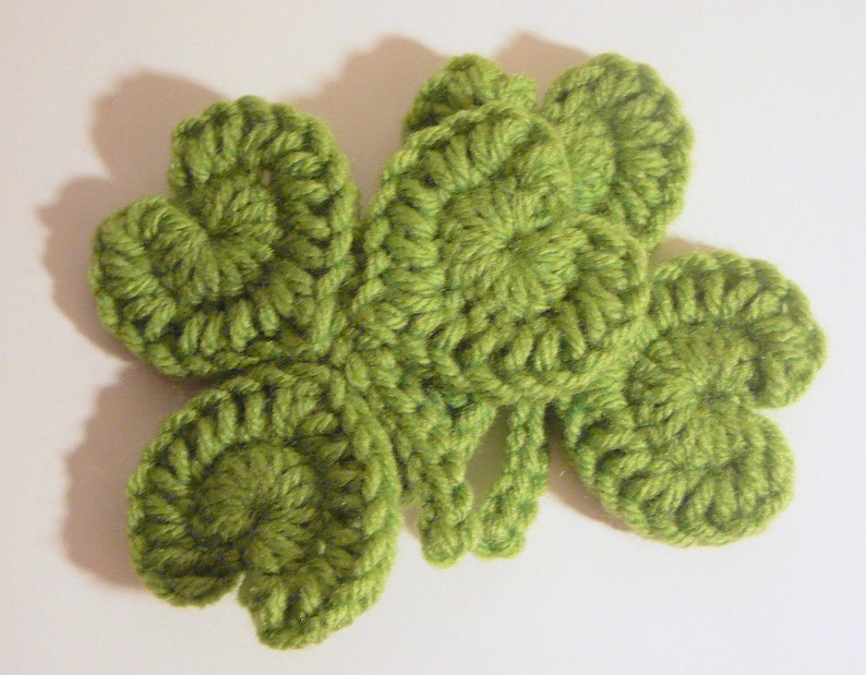 May include: A green crocheted four-leaf clover with a textured design.