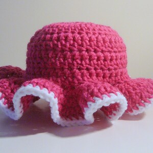 May include: A pink crocheted sun hat with a white crocheted trim around the brim.