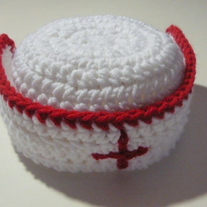 Peut inclure: Chapeau d'infirmière crocheté blanc avec une bordure rouge et une croix rouge sur le devant.
