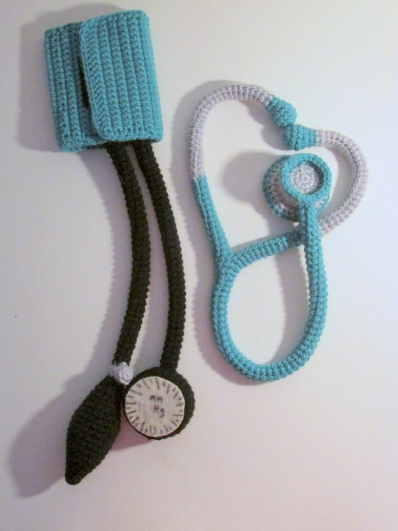 Peut inclure: Un kit de m&eacute;decin en crochet avec un st&eacute;thoscope, un brassard de tension art&eacute;rielle et un manom&egrave;tre. Le st&eacute;thoscope est turquoise et gris, le brassard est turquoise et le manom&egrave;tre est noir et blanc.