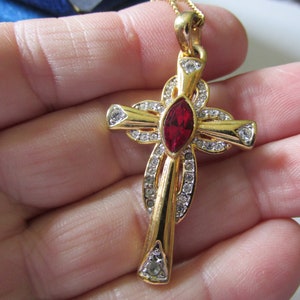 May include: A gold-tone cross pendant necklace with a red rhinestone in the center and clear rhinestones around the edges.