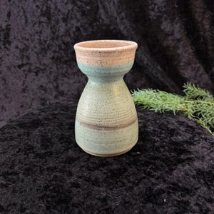 May include: A small, light blue ceramic vase with a speckled glaze and a brown stripe around the middle. The vase has a wide mouth and a narrow base.