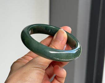 May include: A smooth, dark green jade bangle bracelet. The bangle is polished and has a glossy finish.