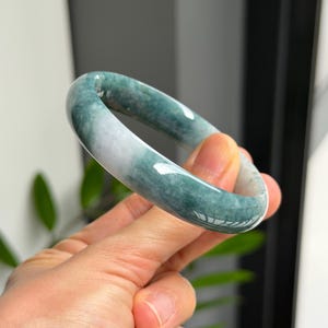 Puede incluir: Una pulsera tipo brazalete lisa y pulida, elaborada en piedra de jade natural. La pieza de joyería circular presenta un patrón variado con secciones de color verde bosque profundo que transicionan hacia áreas blancas lechosas y translúcidas.