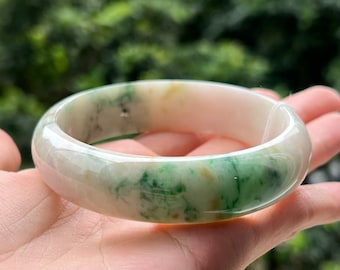 May include: A white jade bangle with green and yellow swirls. The bangle is polished and smooth.