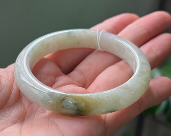 May include: A light green jade bangle bracelet with a smooth, polished finish. The bangle has a subtle, mottled pattern of light green and white.