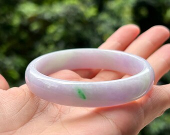 May include: A lavender jade bangle bracelet with a green and white streak. The smooth, polished surface reflects light, showcasing the natural colour variations. This elegant piece of jewellery is a classic accessory.
