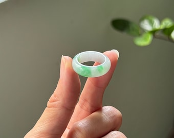 May include: A jade ring with a light green and white color pattern. The ring is round and has a smooth surface.