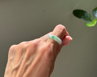 May include: A jade ring with a light green color. The ring is on a person's finger.
