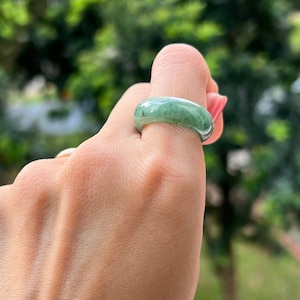 May include: A jade green ring with a smooth, polished finish. The ring is worn on a finger and is a simple, elegant design.