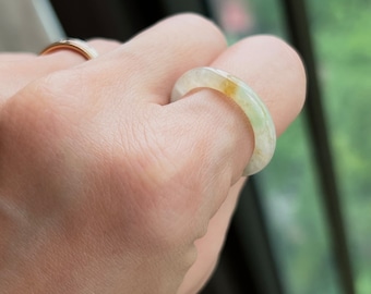 May include: A jade ring with a light green and white color. The ring is thick and has a rounded shape.