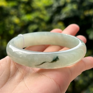 Può includere: Un braccialetto di giada di colore verde chiaro con un motivo a spirale verde scuro.