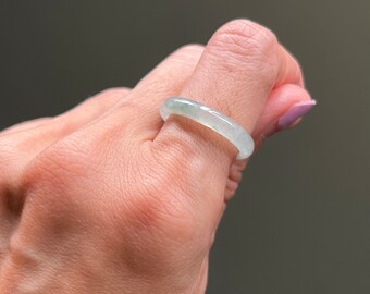 May include: A light green jade ring worn on a finger.