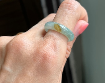 May include: A jade ring with a light green and brown color. The ring is a simple band style.