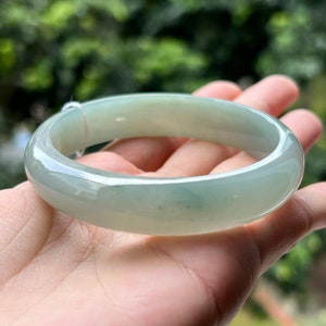 Può includere: Un braccialetto di giada verde chiaro. Il braccialetto è liscio e lucido, con un leggero bagliore.