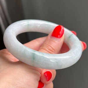 Könnte beinhalten: Ein weißer Jade-Armreif mit grünen Adern. Der Armreif ist glatt und poliert.