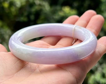 May include: A smooth, lavender jadeite bangle bracelet. The polished stone transitions from a pale green to a soft purple hue. The bracelet is round and appears to be a solid piece of jade.