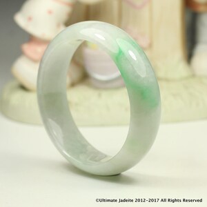 Può includere: Un braccialetto in giadeite di colore verde chiaro con vortici bianchi. Il braccialetto è liscio e lucido.