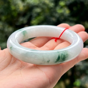 Könnte beinhalten: Ein weißer Jade-Armreif mit grünen Wirbeln und einer glänzenden Oberfläche.