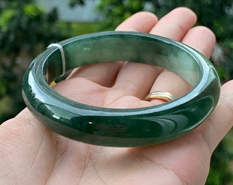 May include: A green jade bangle bracelet. The bangle is smooth and polished, with a dark green color.