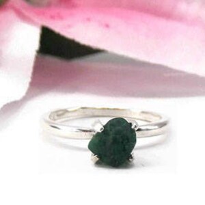 Puede incluir: Un anillo de plata con una piedra preciosa verde oscuro. El anillo est&aacute; sobre un fondo blanco.
