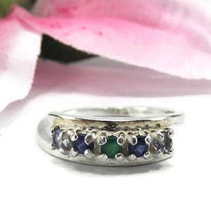 May include: A silver band ring with a row of blue and green gemstones set in a gold band.