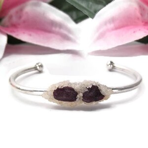 Puede incluir: Un brazalete de plata con dos piedras de cristal morado y blanco.