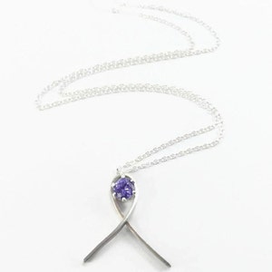 Puede incluir: Un collar de plata con un colgante de piedra preciosa púrpura en forma de cinta.