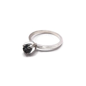 May include: A silver ring with a black gemstone set in a flower-shaped design.