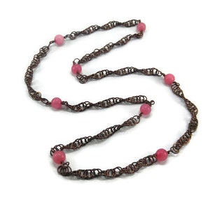 May include: A copper chain necklace with pink beads. The chain is made of small, linked circles that create a twisted, rope-like effect.