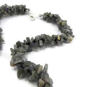 May include: A necklace made of small, irregular, grey labradorite stones strung on black thread. The necklace has a silver clasp.