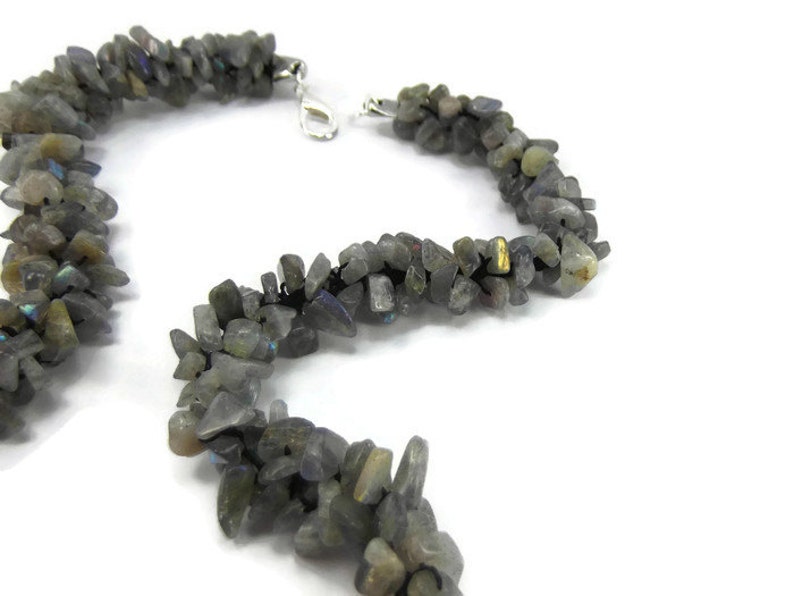 May include: A necklace made of small, irregular, grey labradorite stones strung on black thread. The necklace has a silver clasp.