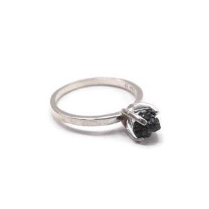 May include: A silver ring with a black rough diamond set in the center.