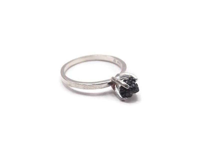 May include: A silver ring with a black rough diamond set in the center.