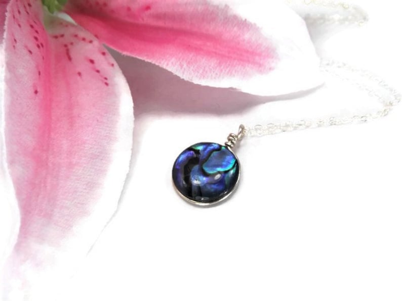 K&ouml;nnte beinhalten: Eine silberne Kettenkette mit einem runden Anh&auml;nger aus Abalone-Muschel. Die Muschel hat schillernde blaue, gr&uuml;ne und violette Farben.