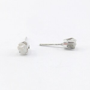 May include: A pair of silver stud earrings with a rough, white diamond in each setting.