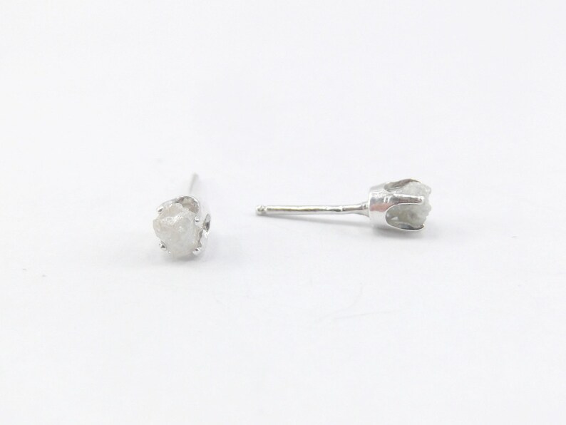 May include: A pair of silver stud earrings with a rough, white diamond in each setting.