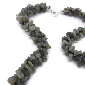 May include: A necklace made of gray labradorite gemstone chips. The chips are irregular in shape and size, and they are strung together on a silver chain.