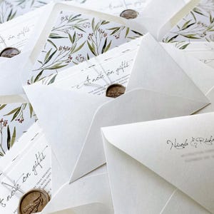 Op de afbeelding: Close-up van witte enveloppen met een bloemmotief aan de binnenkant. Elke envelop is verzegeld met een wasstempel. De tekst "A note on gifts" is zichtbaar op sommige kaarten.