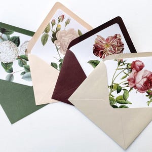 Op de afbeelding: Vier open enveloppen in groen, beige en bordeaux, elk met een bloemenkaart. De kaarten tonen botanische illustraties van rozen en andere bloemen in roze, rood en wit, met groene bladeren.