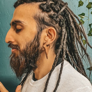 May include: A man with long dreadlocks wears a white sweater and has a wooden earring in his ear.