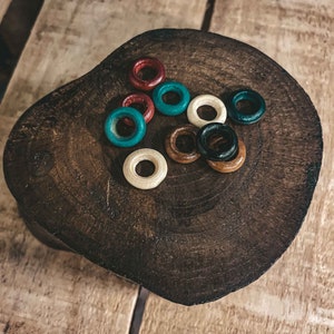 May include: A collection of wooden rings in various colors, including red, blue, white, and black, arranged on a dark brown wooden surface.