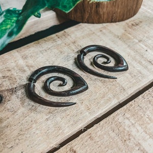 May include: Two dark brown wooden spiral earrings with a unique design. The earrings are made of wood and have a natural finish.